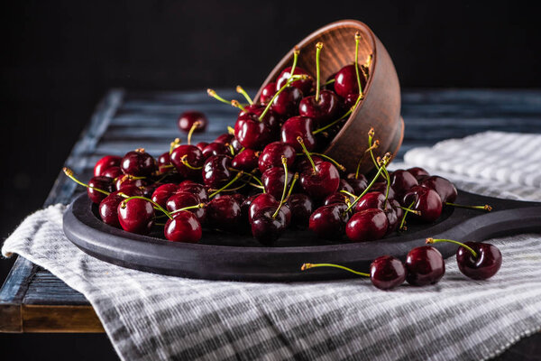 close up view of pile of red ripe cherries in bowl on cutting board on wooden table 