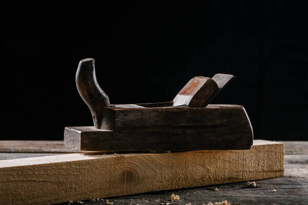  close up view of vintage woodworker plane and plank isolated on black