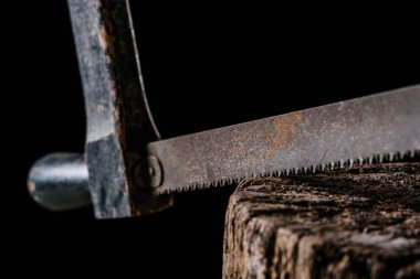  close up view of vintage saw on wooden stump isolated on black clipart