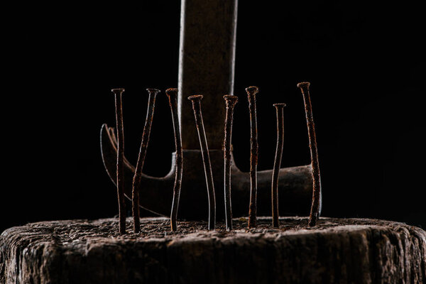  close up view of vintage rusty hammer and nails on wooden stump isolated on black