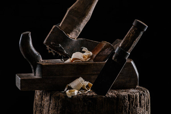 close up view of woodworker plane, axe and chisel carpentry tools on stump isolated on black
