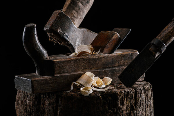 close up view of woodworker plane, axe and chisel carpentry tools on stump isolated on black