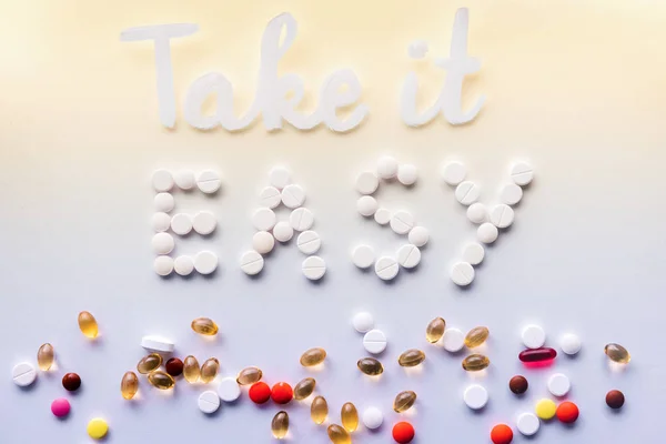 top view of lettering take it easy made by white pills near various tablets on colorful background