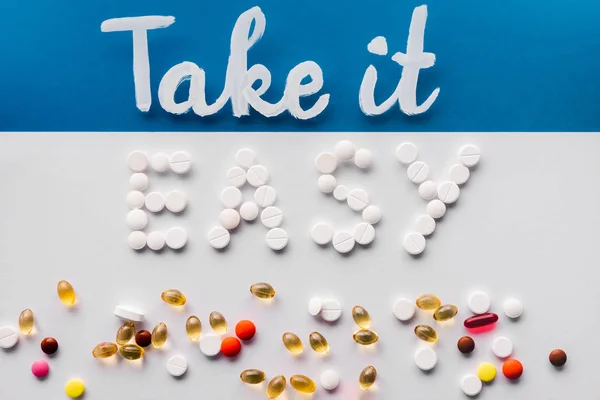 top view of lettering take it easy made by pills near various tablets on colorful background