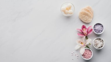 top view of beautiful orchid flowers, sea salt in bowls and sponges on white background 