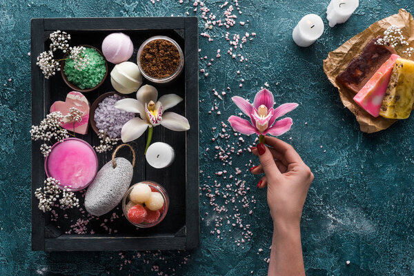 частичный вид сверху лица, держащего цветок орхидеи и органические спа аксессуары в коробке
 