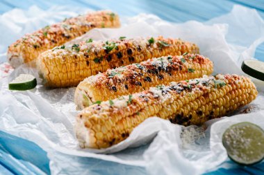 close up view of grilled corn with lime slices on baking paper on wooden table  clipart