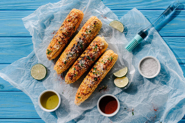 top view of grilled corn, lime slices, cooking brush, oil, salt and chili spice on wooden table 