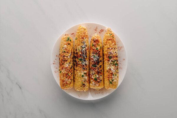 top view of grilled corn with salt and chili spice on plate on marble table 