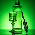 Absinthe bottle with crystal glass and spoon on reflective surface and dark green background