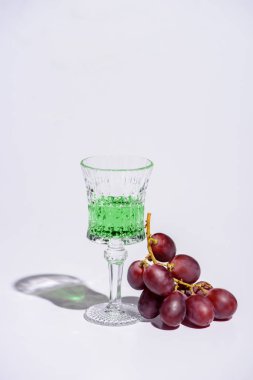 crystal glass of absinthe with branch of grapes on white clipart