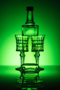 bottle of absinthe with crystal glasses on mirror surface and dark green background clipart