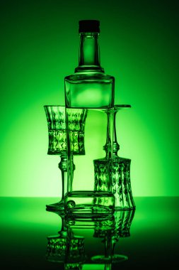 bottle of absinthe with lead glasses on reflective surface and dark green background clipart