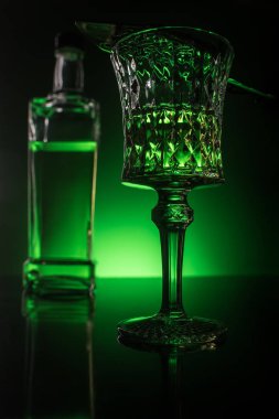 close-up shot of glass with absinthe and bottle on reflective surface and dark green background clipart