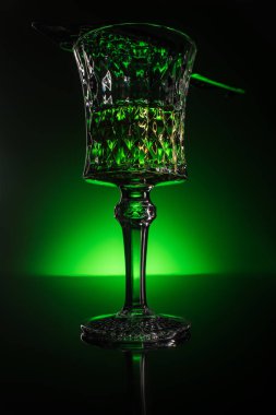 close-up shot of glass with absinthe on reflective surface and dark green background clipart