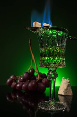 Kristal cam pelin üzüm ve yansıtıcı yüzey ve koyu yeşil zemin üzerine kaşık üzerinde yanan şeker dalı ile