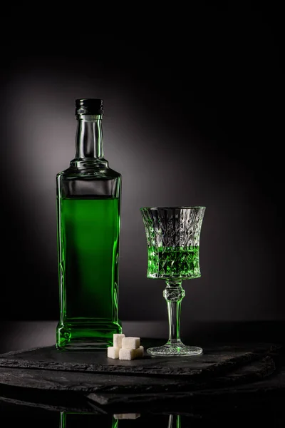 close-up shot of glass and bottle of absinthe with sugar cubes on dark background
