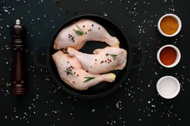flat lay with chicken legs on pan with pepper corns and paprika on black table  clipart