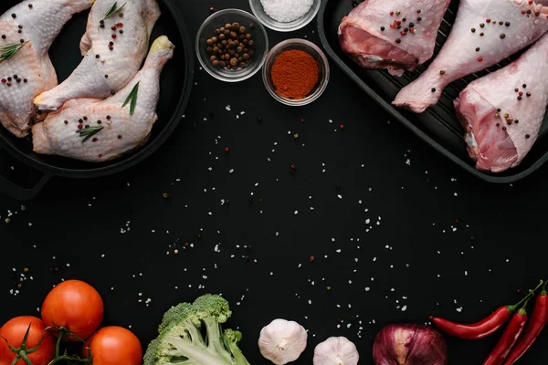 flat lay with chicken and turkey legs in pans with vegetables and spices on dark tabletop