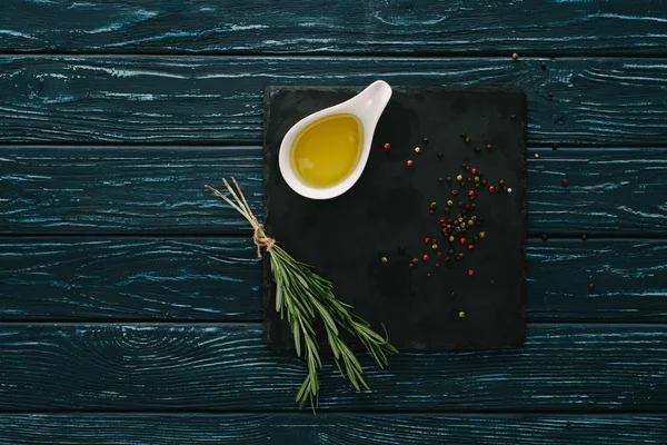 Top view of rosemary, oil and pepper corns black stone slate on wooden tabletop — Stock Image Top View Rosemary Oil Pepper Corns Black Stone Slate Wooden Stock Image