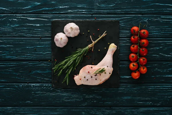 Top view of chicken leg with garlic, rosemary, pepper corns and cherry tomatoes on stone board — Stock Image Top View Chicken Leg Garlic Rosemary Pepper Corns Cherry Tomatoes Stock Photo