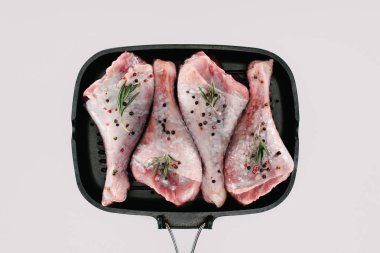 top view of chicken legs with pepper corns, rosemary and salt on grill pan, isolated on white clipart
