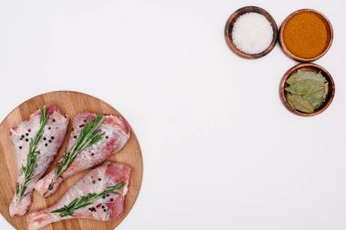 çiğ hindi budu rosemary ile üstten görünüm üzerinde kesme tahtası üzerinde beyaz izole kase, tuz, kırmızı biber ve defne yaprakları ile