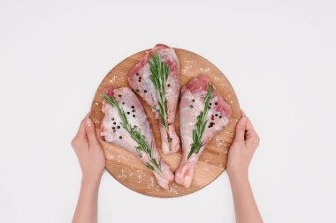 cropped view of woman holding wooden cutting board with turkey legs and rosemary, isolated on white  clipart