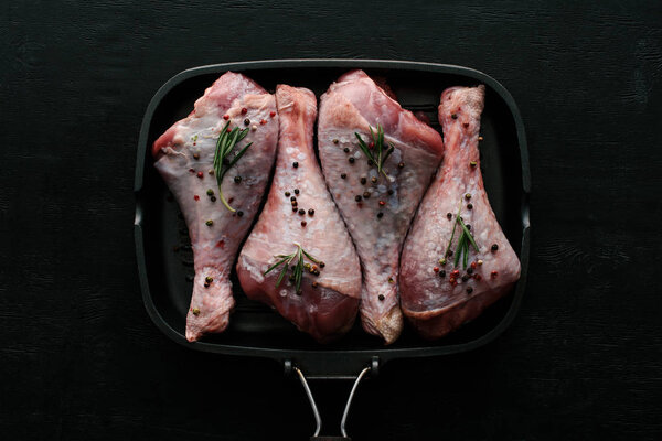 top view of chicken legs with pepper corns and rosemary in grill pan on black wooden table