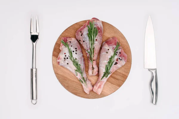 顶部视图的原始火鸡腿胡椒玉米和迷迭香在切割板上的叉子和刀 孤立的白色 — 图库照片