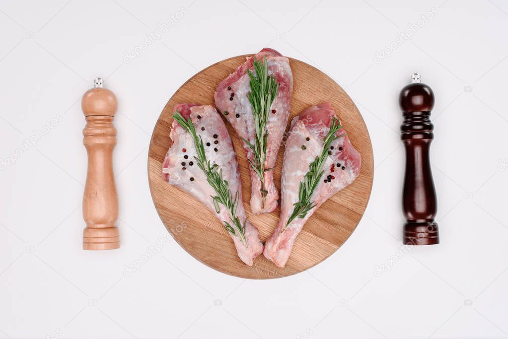 top view of uncooked turkey legs with rosemary, pepper and salt, isolated on white
