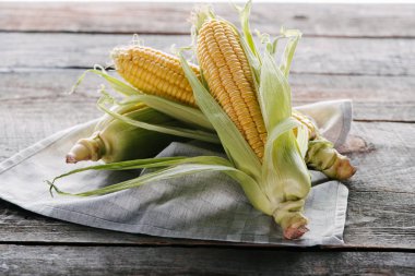 close up view of raw corn cobs on linen arranged on wooden surface clipart