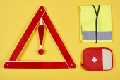 top view of warning triangle road sign, first aid kit and reflective vest isolated on yellow