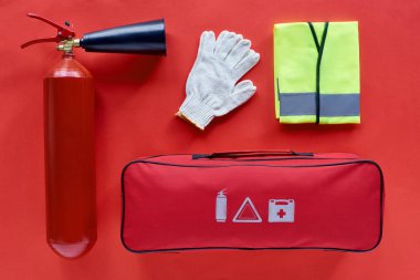 kırmızı zemin üzerine otomotiv el çantası, yansıtıcı yelek, eldiven ve yangın söndürücü üstten görünüm