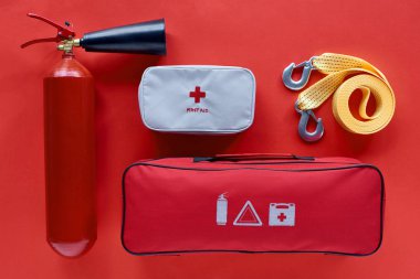 flat lay with fire extinguisher, automotive handbag, first aid kit and car tow rope on red backdrop clipart