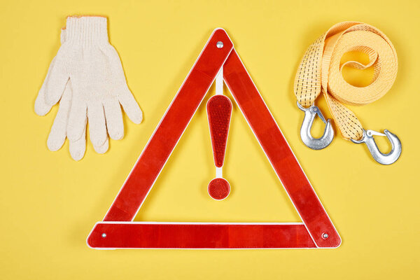 вид сверху на предупреждающий треугольник дорожный знак, перчатки и веревку для эвакуации автомобиля изолированы на желтый
