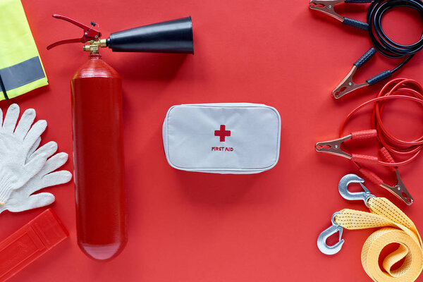 flat lay with fire extinguisher, first aid kit and automotive accessories on red background