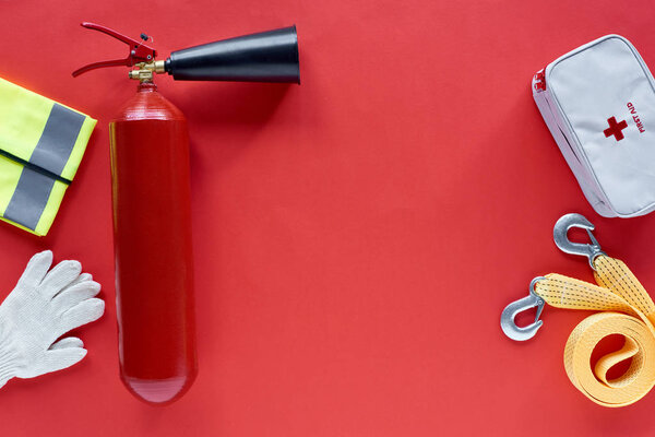 flat lay with fire extinguisher, first aid kit and automotive accessories on red background