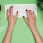 女性建筑师在桌上用咖啡、植物和分切器打字的计算机键盘上的裁剪图像