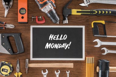 top view of blackboard with lettering hello monday near arranged various tools on wooden table clipart