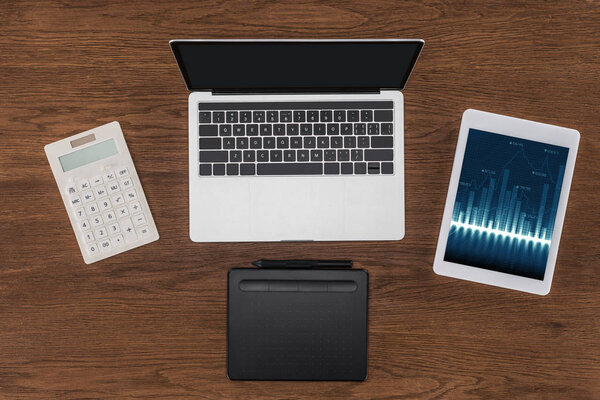 top view of laptop with blank screen, calculator, textbook and digital tablet with graphics on screen 