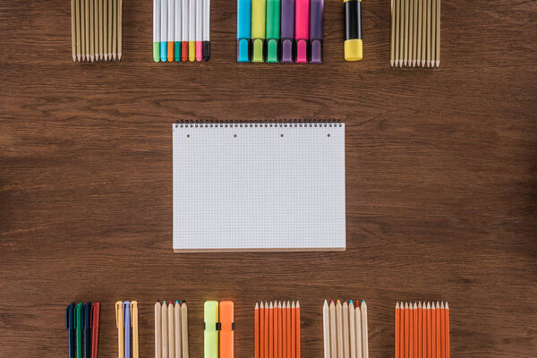 top view of empty textbook near arranged various pencils and markers on wooden table 