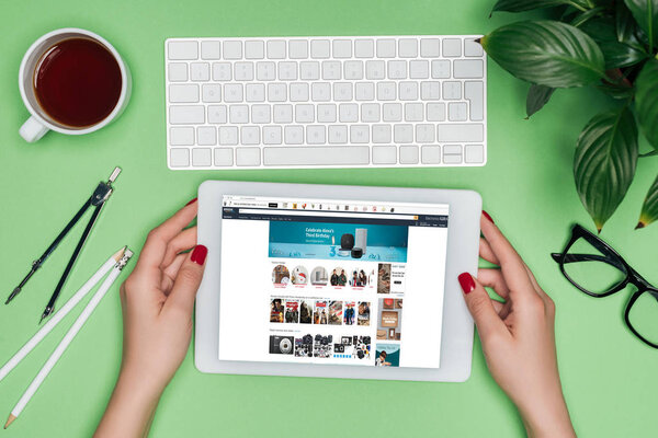 обрезанное изображение женщины-архитектора с цифровым планшетом с амазонином на экране за столом с разделителем, очками и растением в горшке
 