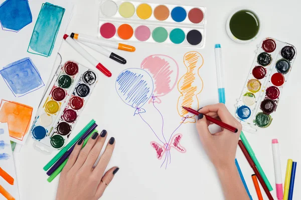 cropped image of female artist drawing air balloons at white table with colorful paints