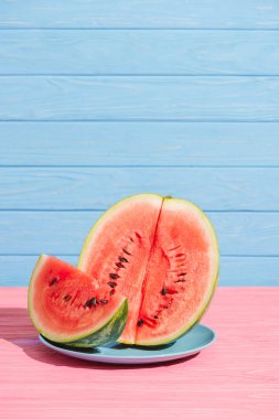 close up view of cut juicy watermelon on plate on pink tabletop on blue backdrop clipart