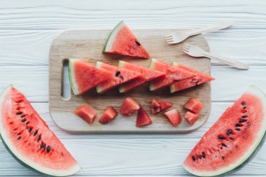 düz lay ile düzenlenmiş karpuz parçalar kesme tahtası üzerinde ve ahşap masa üzerinde plastik çatal bıçak takımı