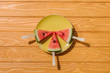 flat lay with watermelons on ice cream sticks on plate on wooden tabletop clipart