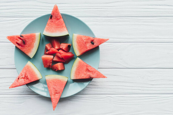 top view of fresh watermelon pieces on plate on white wooden surface