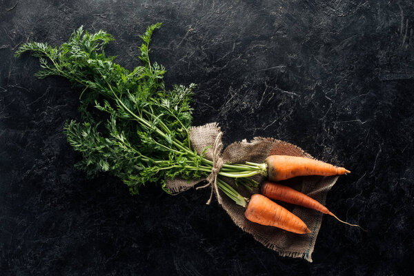 top view of fresh ripe carrots tied with rope on sackcloth on black marble surface