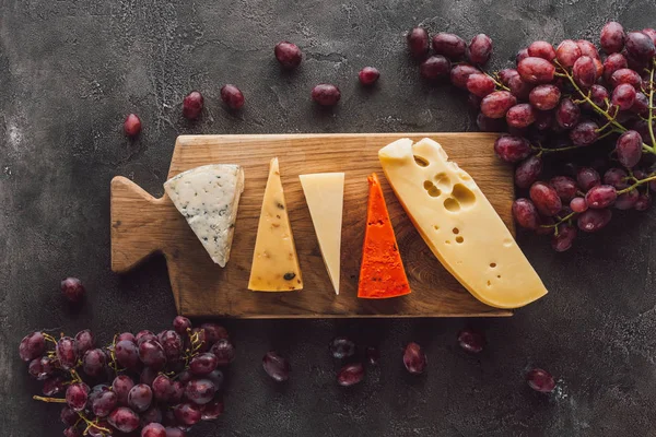 Üzüm Karanlık Yüzeyi Ile Ahşap Kesme Tahtası Üzerinde Çeşitli Peynir — Stok fotoğraf
